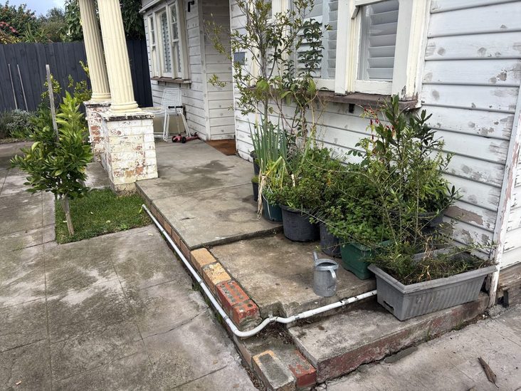 Cracked concrete verandah with weeds and pot plants, before the deck went in