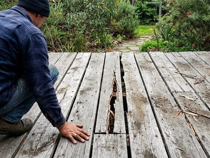 A man checking a split board on an old weathered deck