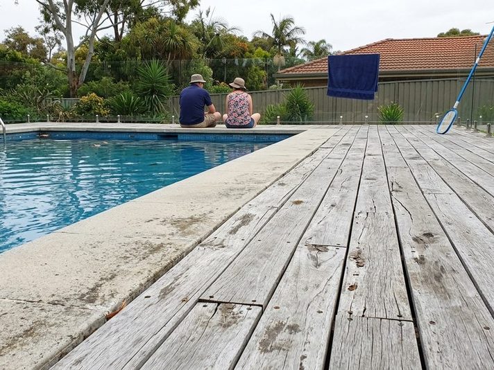 Two children sitting beside a pool ringed with tired grey timber