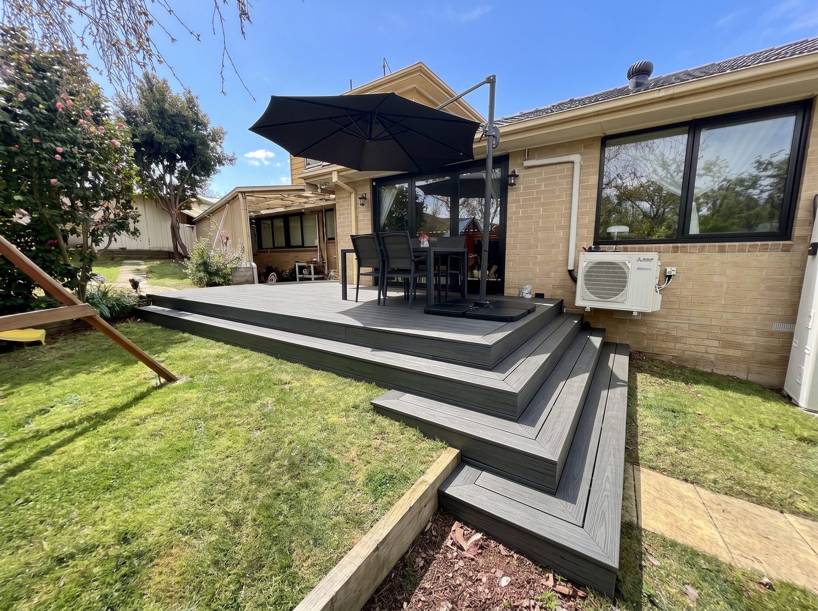 Grey composite deck with wide steps wrapping two sides down to the lawn