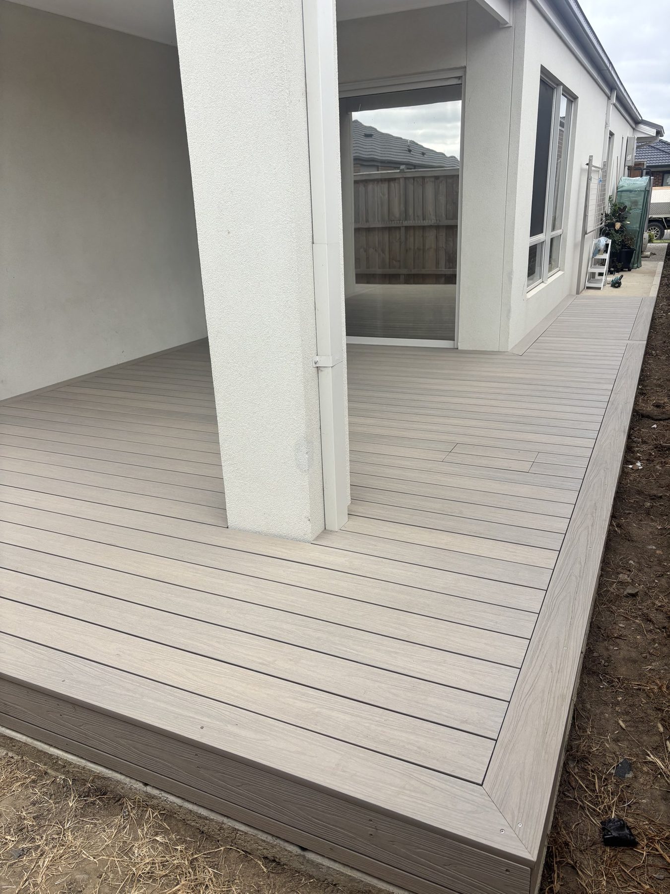 Pale composite decking on a new build, boards cut clean around a rendered post