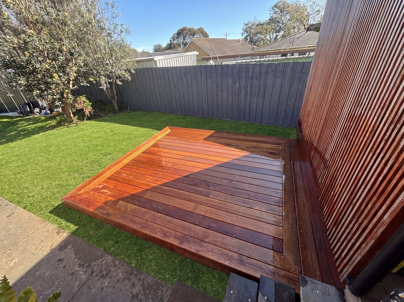 Merbau deck freshly oiled, deep red, against a slatted timber screen
